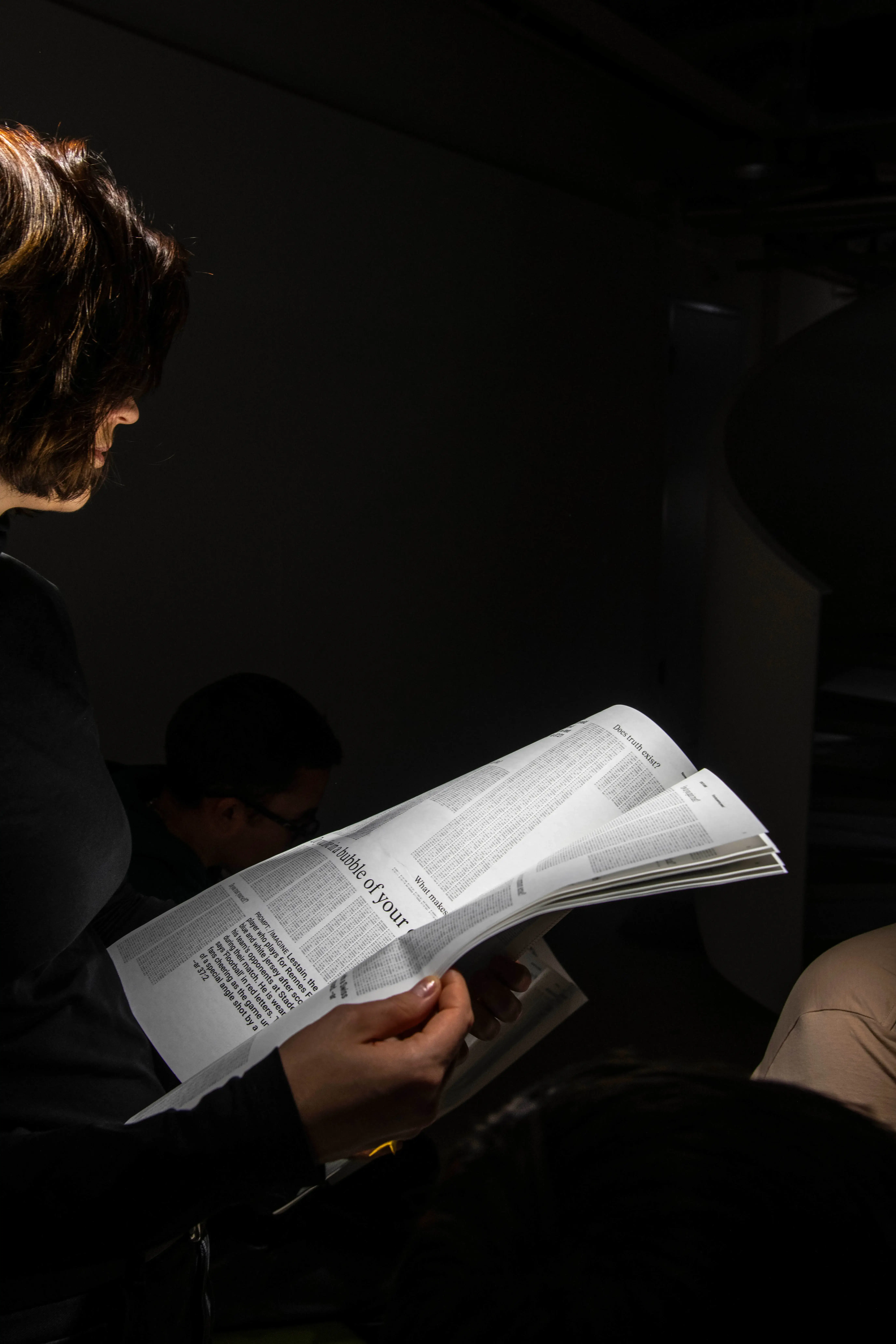 person dark background looking at newspaper